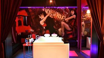 Une pièce avec une baignoire, un mur rouge orné d’une fresque et une petite table avec une lampe.