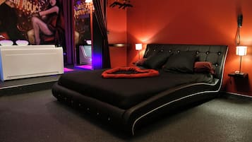 Un dormitorio moderno con cama negra, manta roja y un cartel en la pared.
