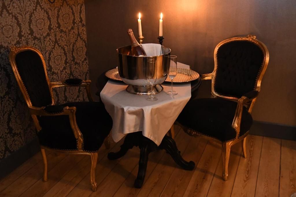 A dining table with a metal centerpiece, two chairs, and candles.