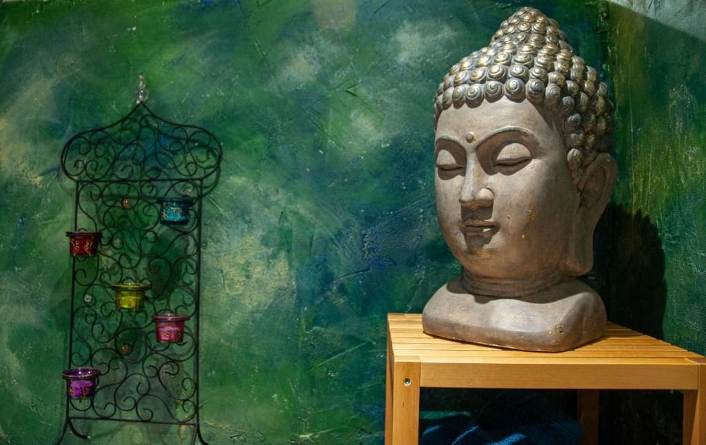 Une statue de Bouddha, posée sur un piédestal en bois, se détache sur un mur vert.
