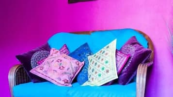 Un sofá de mimbre con un cojín azul frente a una pared rosa, junto con un cuadro con la imagen de un elefante.