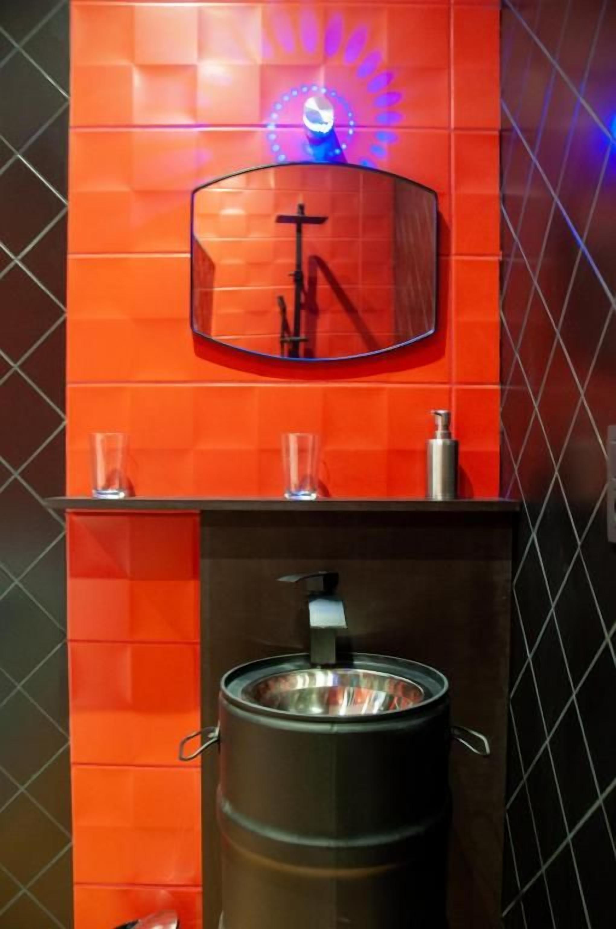 Une salle de bain avec un grand miroir, un lavabo et un récipient en acier inoxydable.
