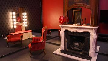 Ein Zimmer mit Spiegel, Schminktisch, roten Stühlen, Kamin und roter Wand.