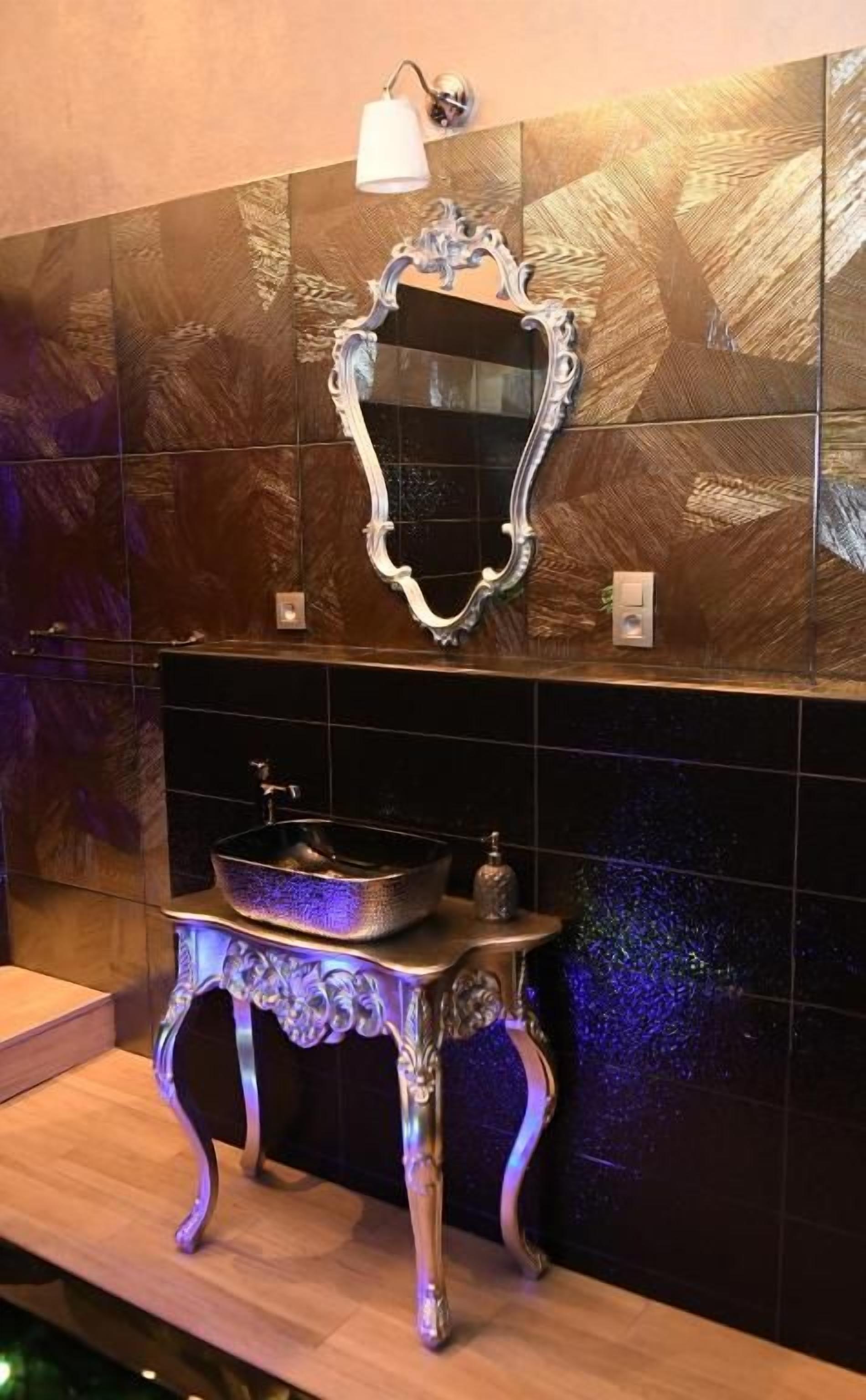Une salle de bain avec un miroir décoratif, un lavabo et un mur orné d’un motif texturé.