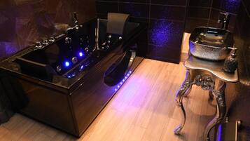 Une salle de bain avec une baignoire noire, un plancher en bois et un lavabo agrémenté d’un récipient décoratif.