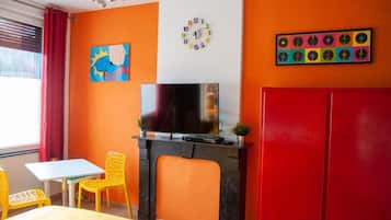 A room with a bed, a TV, a fireplace, a red wardrobe, a painting, and a clock on the wall.