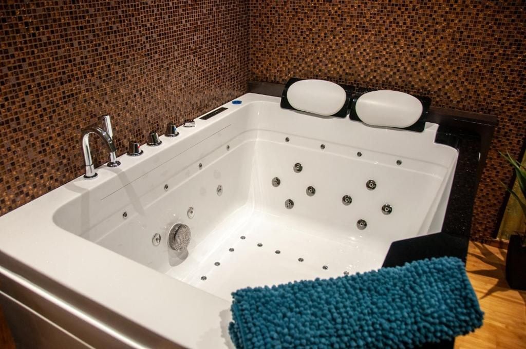 Ein modernes Badezimmer mit einer großen, weißen Badewanne, einem chromfarbenen Wasserhahn und einer blauen Badematte.