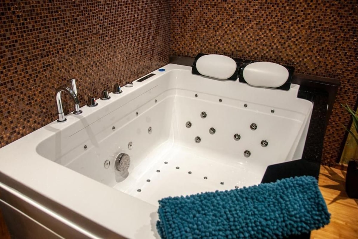 A modern bathroom with a large white bathtub, a chrome faucet, and a blue bath mat.