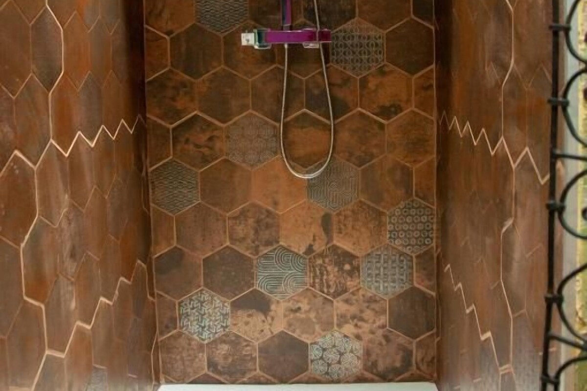 A shower area with a hexagonal patterned wall, a handheld showerhead, and a wall-mounted faucet.