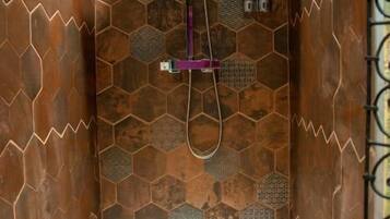 En duschhörna med en vägg som har ett hexagonalt mönster, ett duschmunstycke som kan hållas i handen och en väggmonterad blandare.