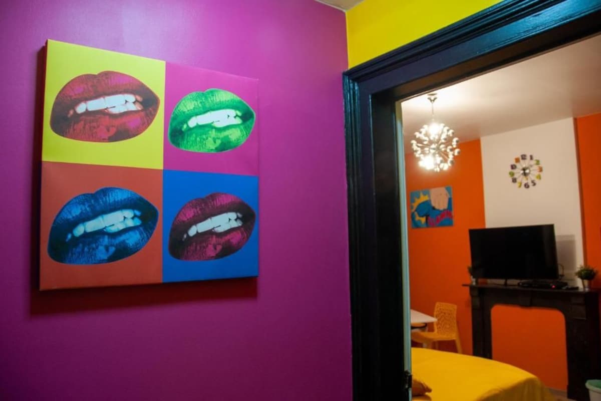 Una habitación con una llamativa obra de arte en la pared, un televisor y una cama con cubierta amarilla.