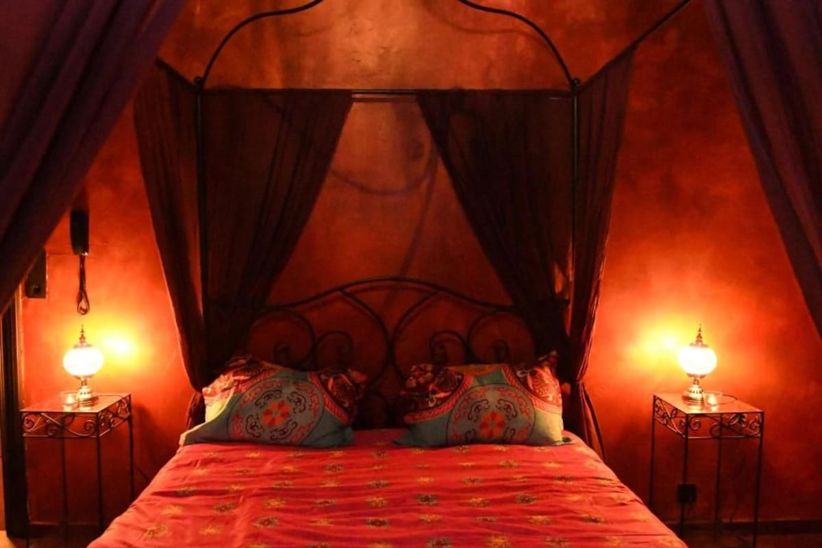 A four-poster canopy bed with ornate headboard, two bedside lamps, and patterned pillows.
