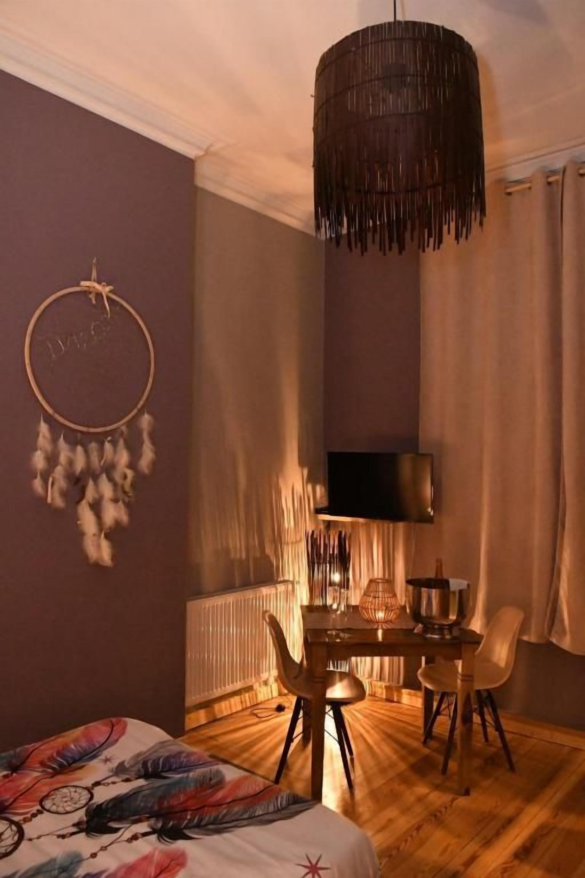 Una habitación con cama, escritorio, silla, lámpara colgante y televisor en la pared.