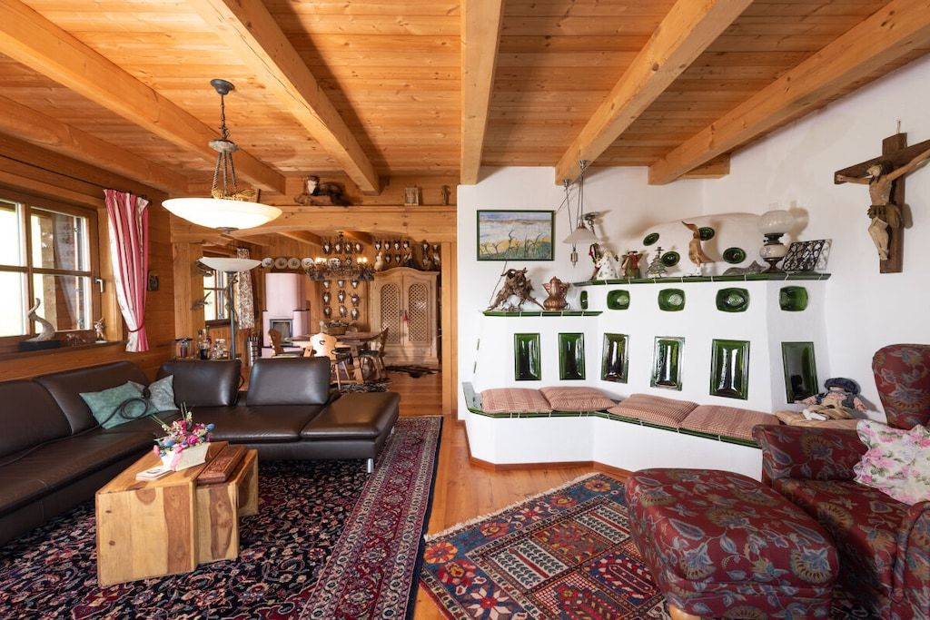 Ein gemütliches Wohnzimmer mit Holzboden, einer schwarzen Ledercouch, einem gemusterten Teppich und einem an der Wand befestigten Regal mit dekorativen Gegenständen.