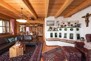 A cozy living room with a wooden ceiling, a black leather sofa, a patterned rug, and a wall-mounted shelf with decorative items. - Kraxlhütte Carinthia (Dröschitz)