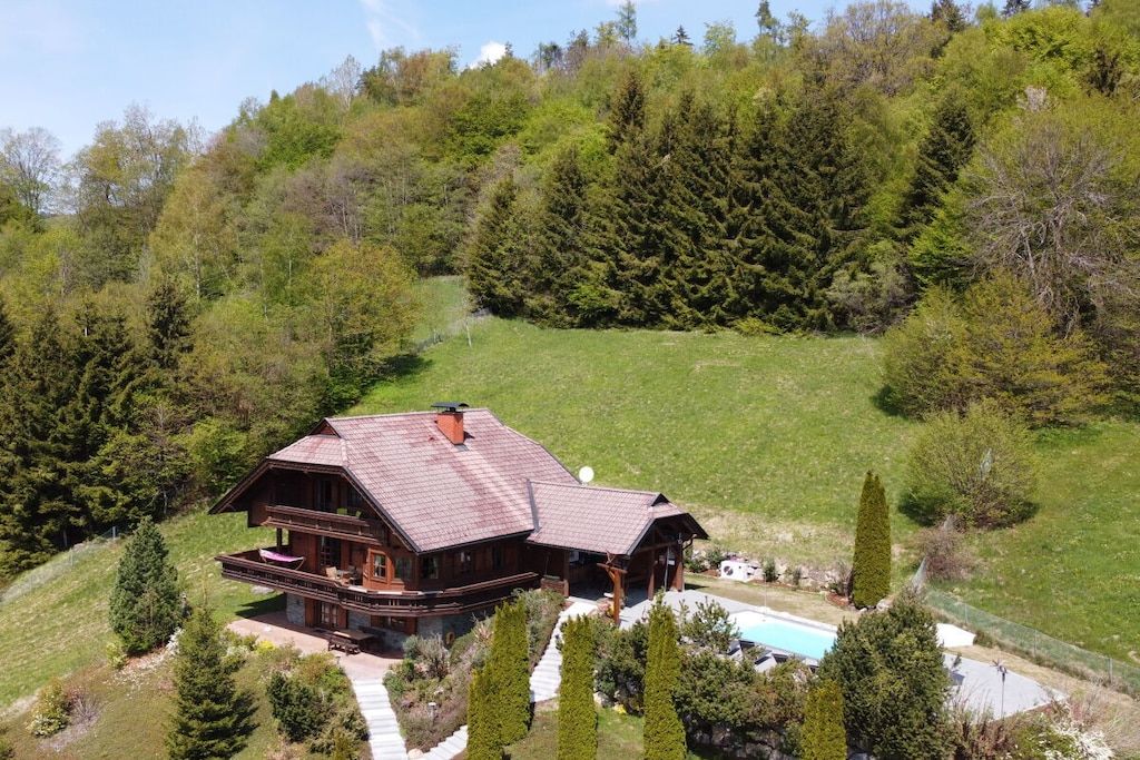 A large wooden cabin with a balcony, surrounded by a grassy area and trees.