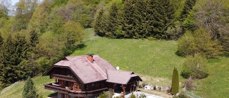 A large wooden cabin with a balcony, surrounded by a grassy area and trees.