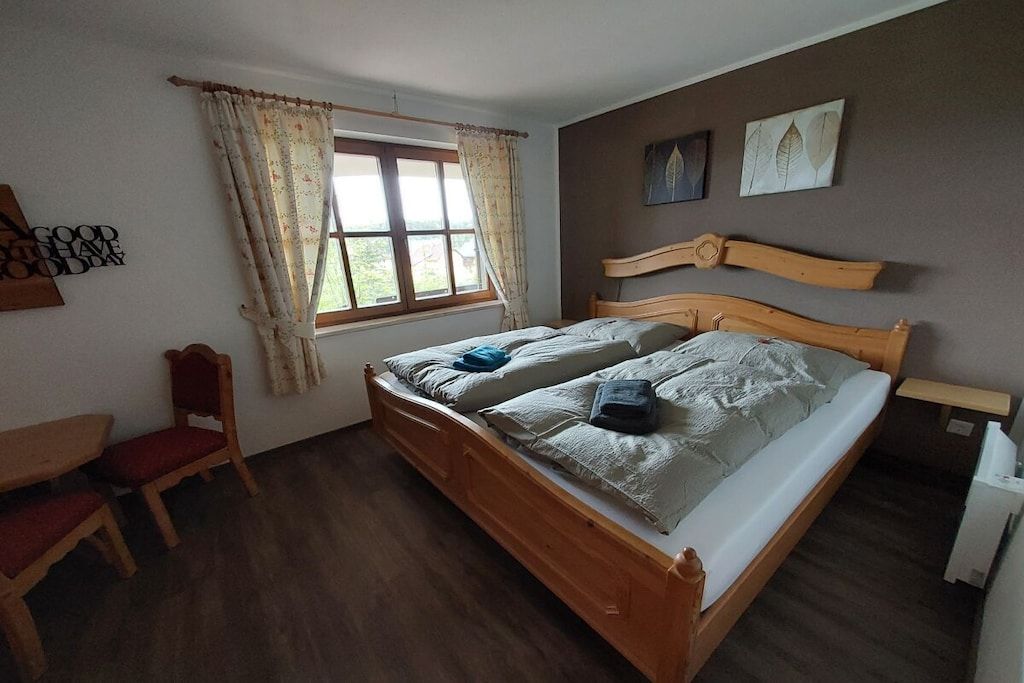 A bedroom with a wooden bed, a window with curtains, a chair, and a wall with leaf-patterned artwork.