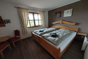 Quarto com cama de madeira, janela com cortinas, uma cadeira e uma parede com arte de padrão de folhas.