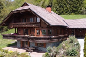 A two-story log cabin with a balcony, stone foundation, and a wooden deck. - Kraxlhütte Carinthia (Dröschitz)