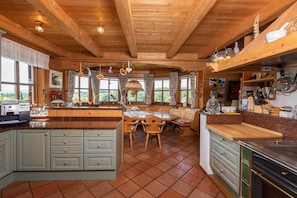 A spacious kitchen with wooden beams, a central island, and a dining area with chairs. - Kraxlhütte Carinthia (Dröschitz)