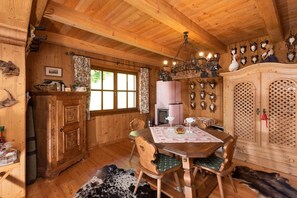 A wooden interior with a dining table, chairs, a chandelier, and a cabinet with decorative items. - Kraxlhütte Carinthia (Dröschitz)