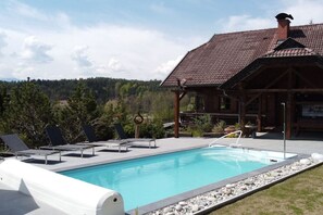Une piscine avec des chaises longues, un chalet en bois et un paysage boisé en arrière-plan.