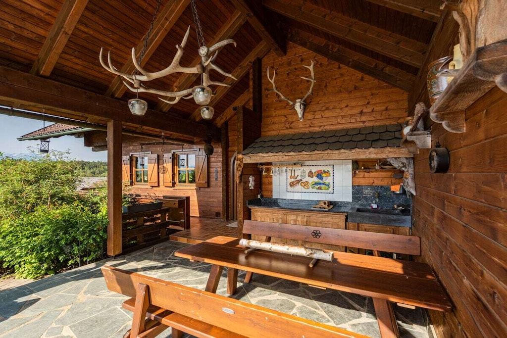 A rustic wooden cabin with a stone patio, wooden benches, and antler decorations.