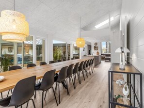 Moderni ruokailutila, jossa on pitkä puinen pöytä, mustat tuolit ja kaksi riippuvalaisinta.