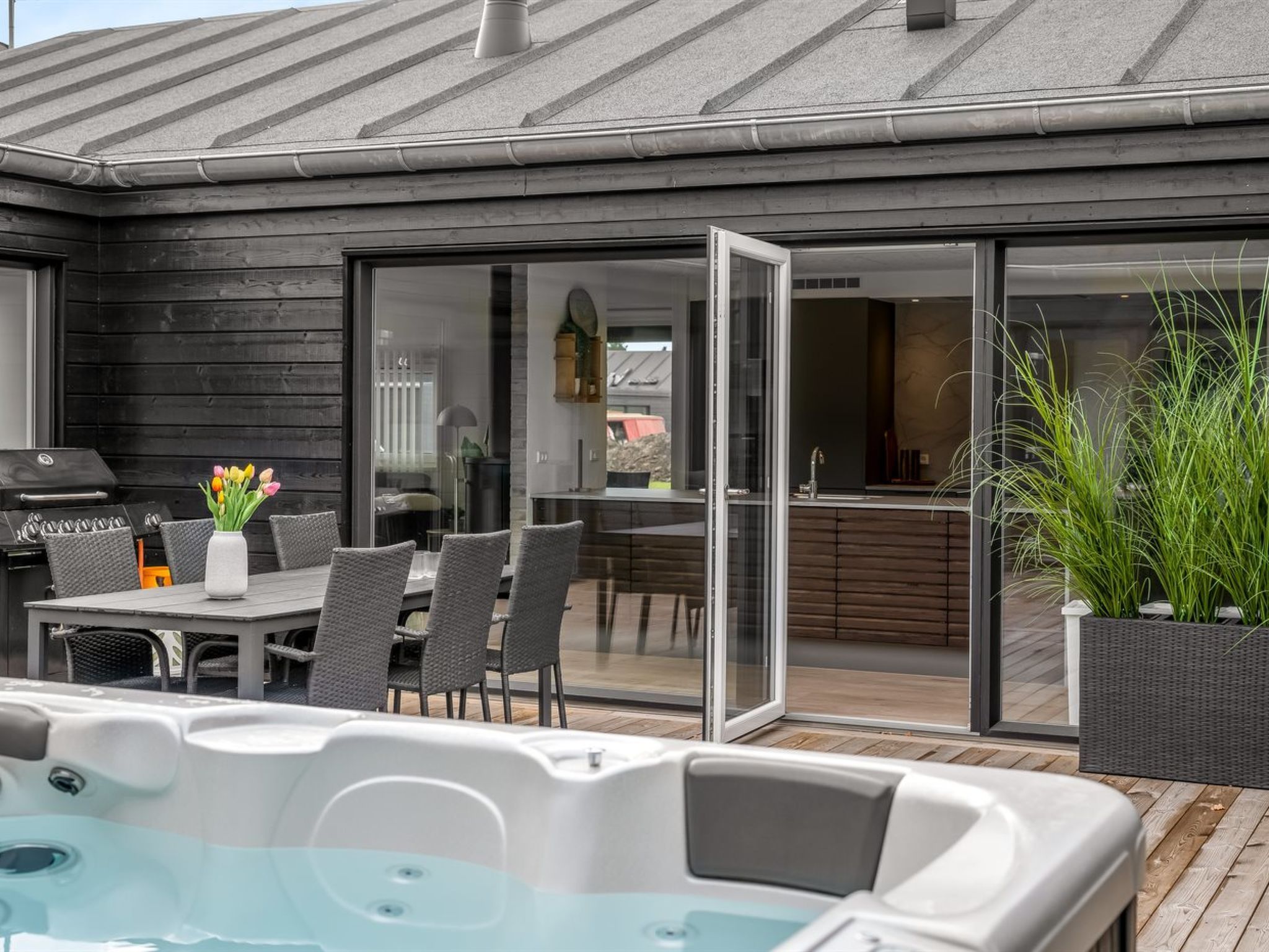 An outdoor patio with a hot tub, dining area, and a sliding glass door leading to a kitchen.