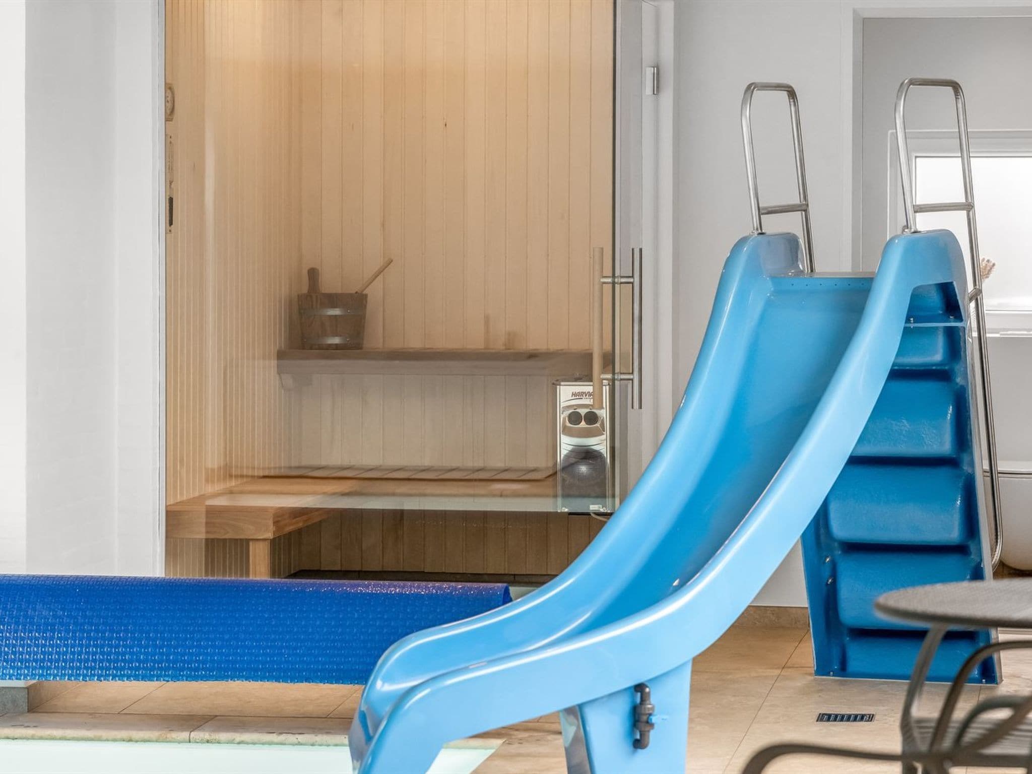 A blue slide in a pool area with a sauna and a wooden bench.