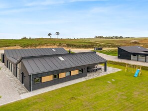 Un bâtiment moderne doté d’un toit plat, de grandes fenêtres et d’un patio aménagé avec des sièges extérieurs.