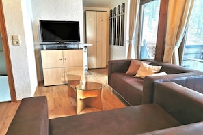 Een moderne woonkamer met een flatscreen televisie, een glazen salontafel, leren banken en een kledingkast.