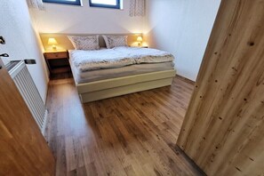 Een slaapkamer met een bed, twee bedlampjes, een radiator en een houten vloer.