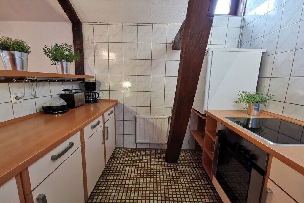 Eine kleine Küche mit Fliesenboden, Holzschränken, einem eingebauten Backofen und einem weißen Kühlschrank.
