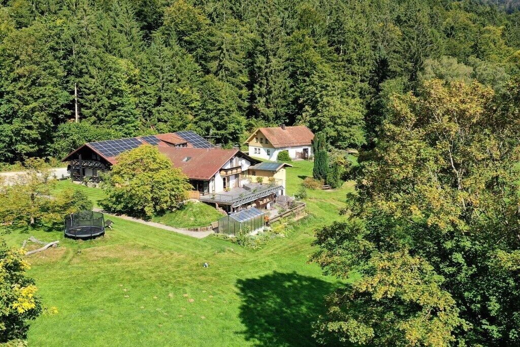 Il s’agit d’une propriété résidentielle comprenant plusieurs bâtiments, dont une maison équipée de panneaux solaires, le tout entouré d’une végétation luxuriante et d’une zone boisée.