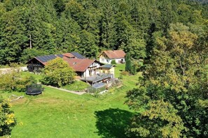 Ein Wohnanwesen mit mehreren Gebäuden, darunter ein Haus mit Solaranlage, umgeben von üppiger Vegetation und einem Waldgebiet.