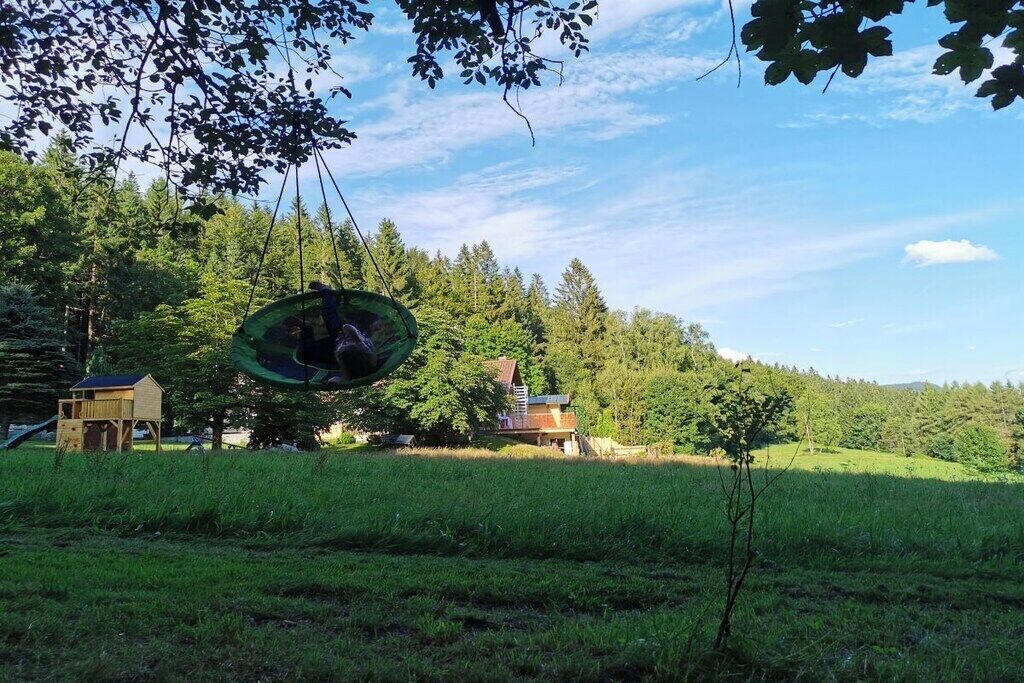A rural landscape with a house, a swing set, and a forest in the background.