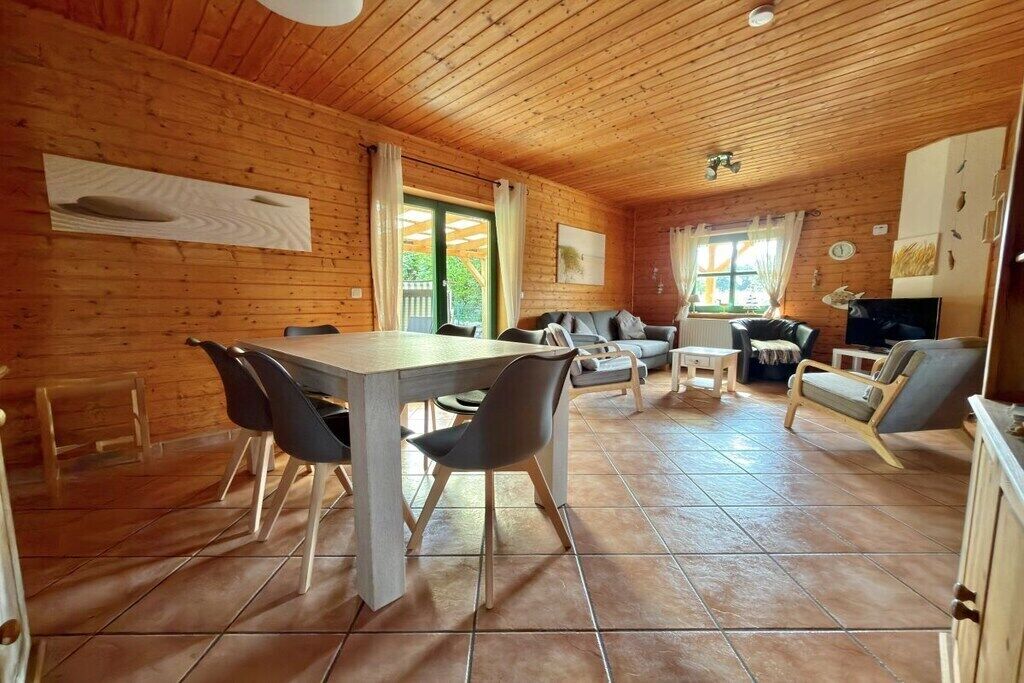 Interior de una cabaña de madera con una mesa de comedor, sillas, un sofá y un televisor.