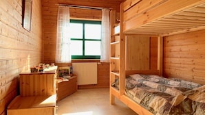 Une chambre dans un chalet en bois, avec un lit superposé, un petit bureau et une fenêtre avec des rideaux.