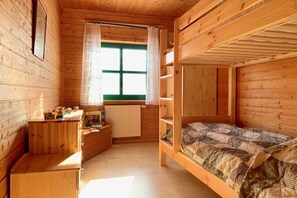 Een houten kamer met een stapelbed, een klein bureau en een raam met gordijnen.