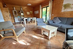 Ein gemütliches Wohnzimmer mit einer Couch, Sesseln und einem Couchtisch. Im Hintergrund ist ein Essbereich mit Tisch und Stühlen zu sehen.