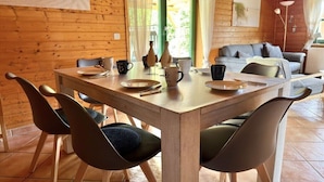 Un intérieur en bois avec une table à manger dressée pour quatre personnes, des chaises, un canapé et une lampe.