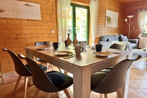 Een houten interieur met een eettafel voor vier personen, stoelen, een bank en een lamp.