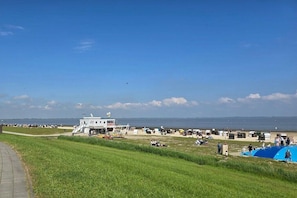 A coastal area with a white building, a grassy field, and a beach with people and tents. - "Little Friesian" Dangast (Varel Dangast)
