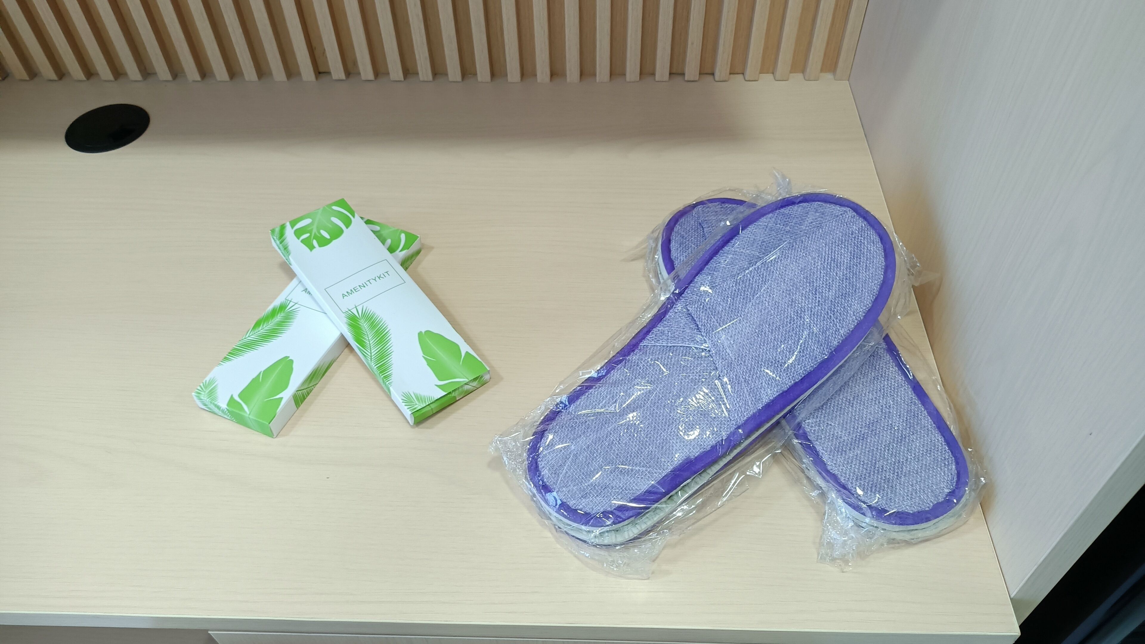 A wooden drawer with a black circular object, a white box with green leaf patterns, and two purple items wrapped in plastic.
