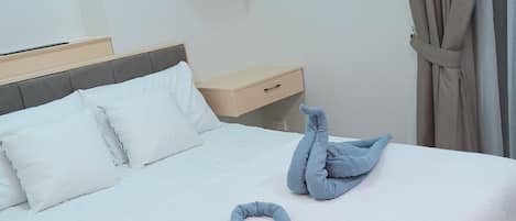 A hotel room with a bed, pillows, a nightstand, a small table, a wall-mounted air conditioner, and a window with curtains.
