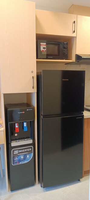 Eine kleine Küche mit einem schwarzen Kühlschrank, einem Wasserspender und einer Mikrowelle auf einem Regal.
