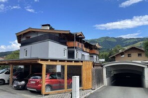 Ein modernes, zweistöckiges Gebäude mit überdachtem Parkplatz und Blick auf die umliegenden Hügel.