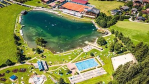 An aerial view of a lakeside property with a swimming pool, tennis courts, and a large building with a red roof. - Mountain view - Kirchberg Center (Kirchberg)